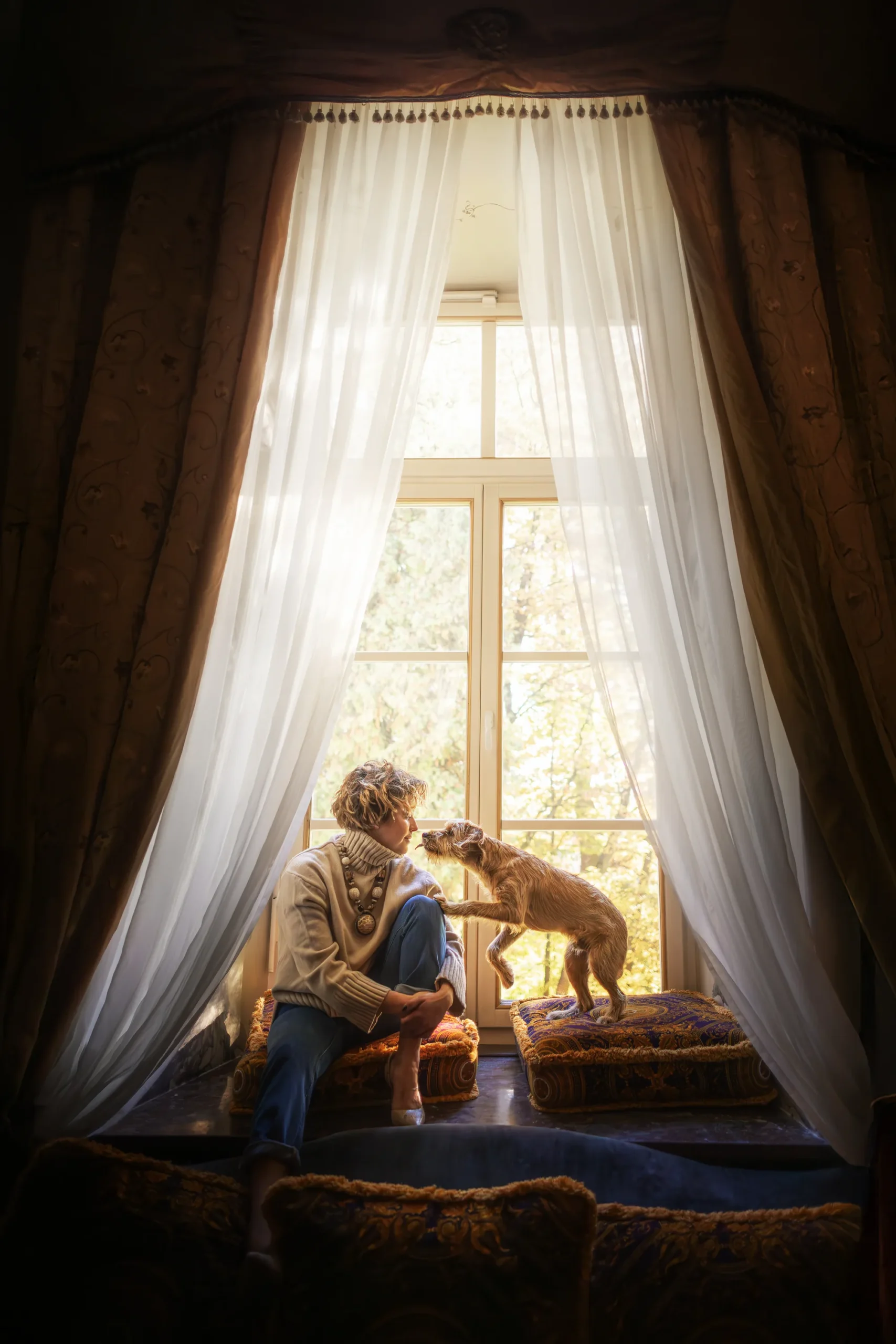 Agnieszka Janarek sitting beside her tan dog on cushions in a sunlit window